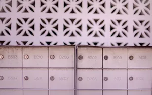 Two banks of numbered metal mailboxes set against a patterned white breeze-block wall.