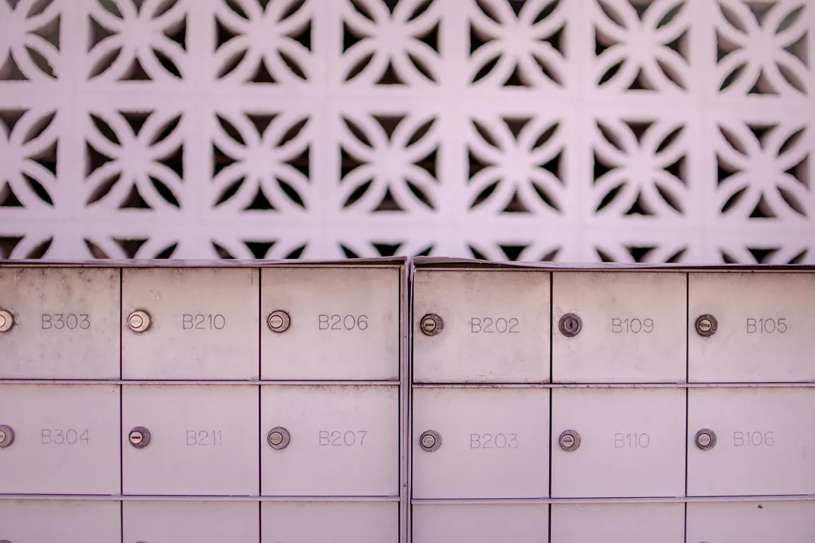 Two banks of numbered metal mailboxes set against a patterned white breeze-block wall.